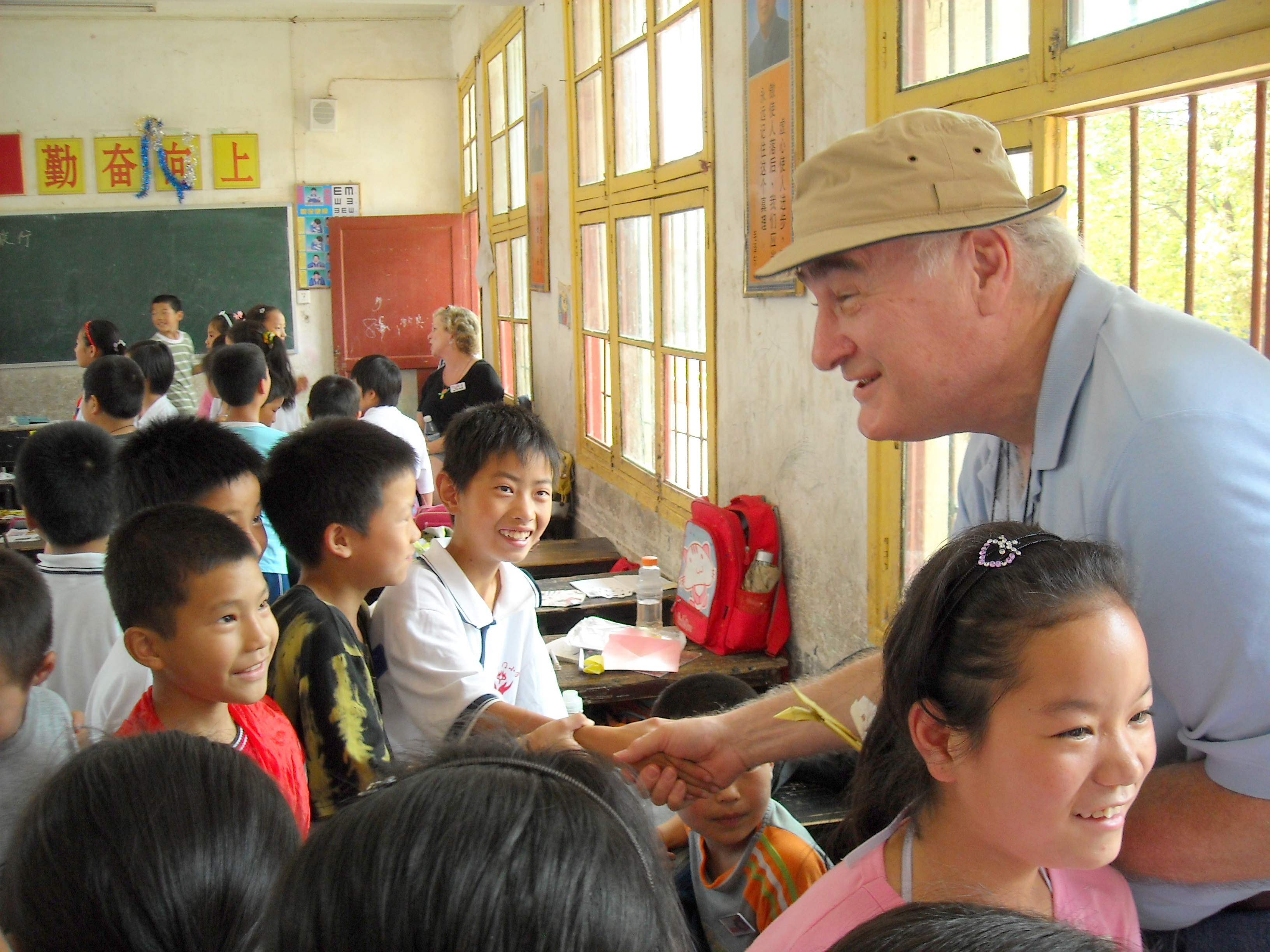 An American man shakes hands with several Asian children at their school.