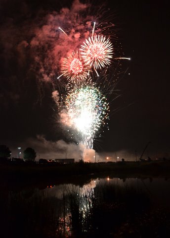 Red and white fireworks against a black sky and pond
